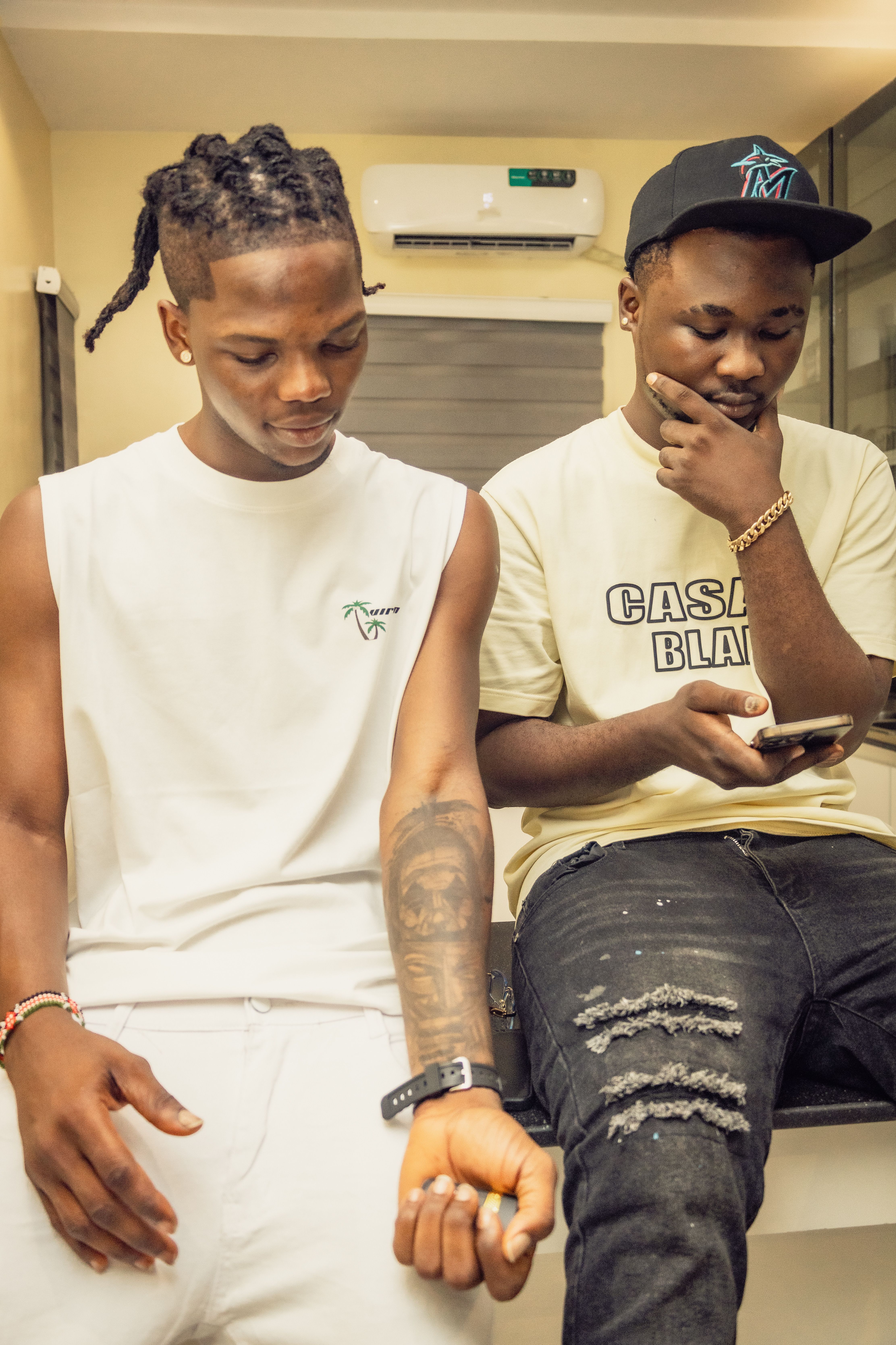 Two young men in casual urban fashion indoors, engaging with a smartphone.