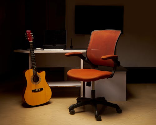 A Guitar Standing next to a Desk with a Computer 