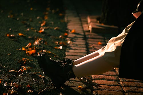 Close-up of Legs of a Woman Wearing a Dress and Boots and Sitting Outside in Autumn 
