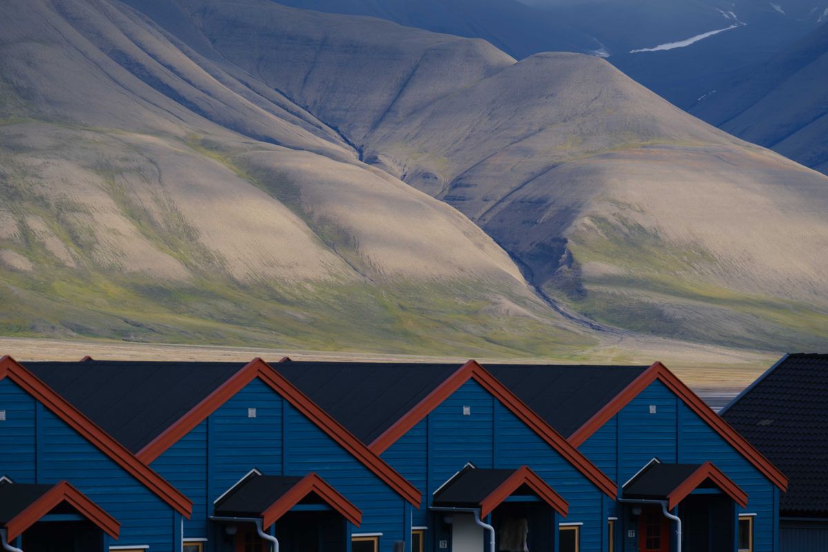 Longyearbyen's blue houses with red roofs, raised above the permafrost, backed by a bare mountain streaked with old snow.