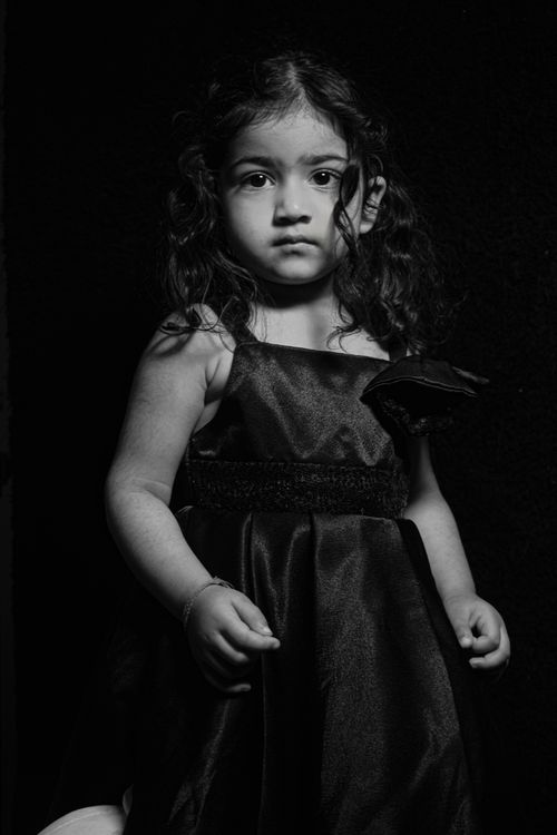 Free Expressive black and white portrait of a young girl in a dress against a dark background. Stock Photo
