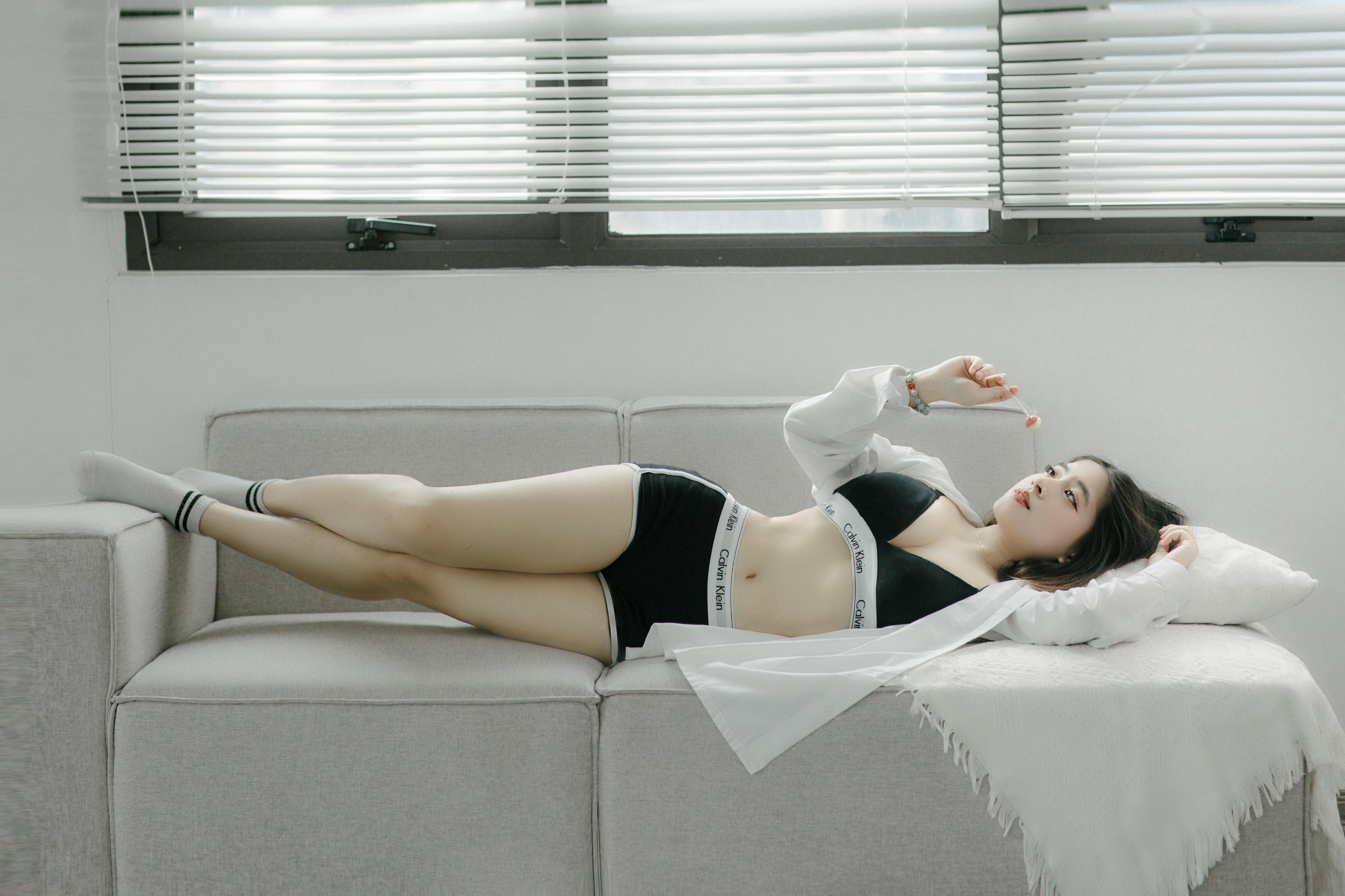 An adult woman poses stylishly indoors on a sofa, exuding tranquil elegance.
