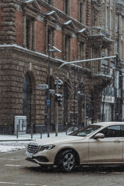 Free A luxury sedan navigating through a snowy intersection in an urban cityscape during winter. Stock Photo