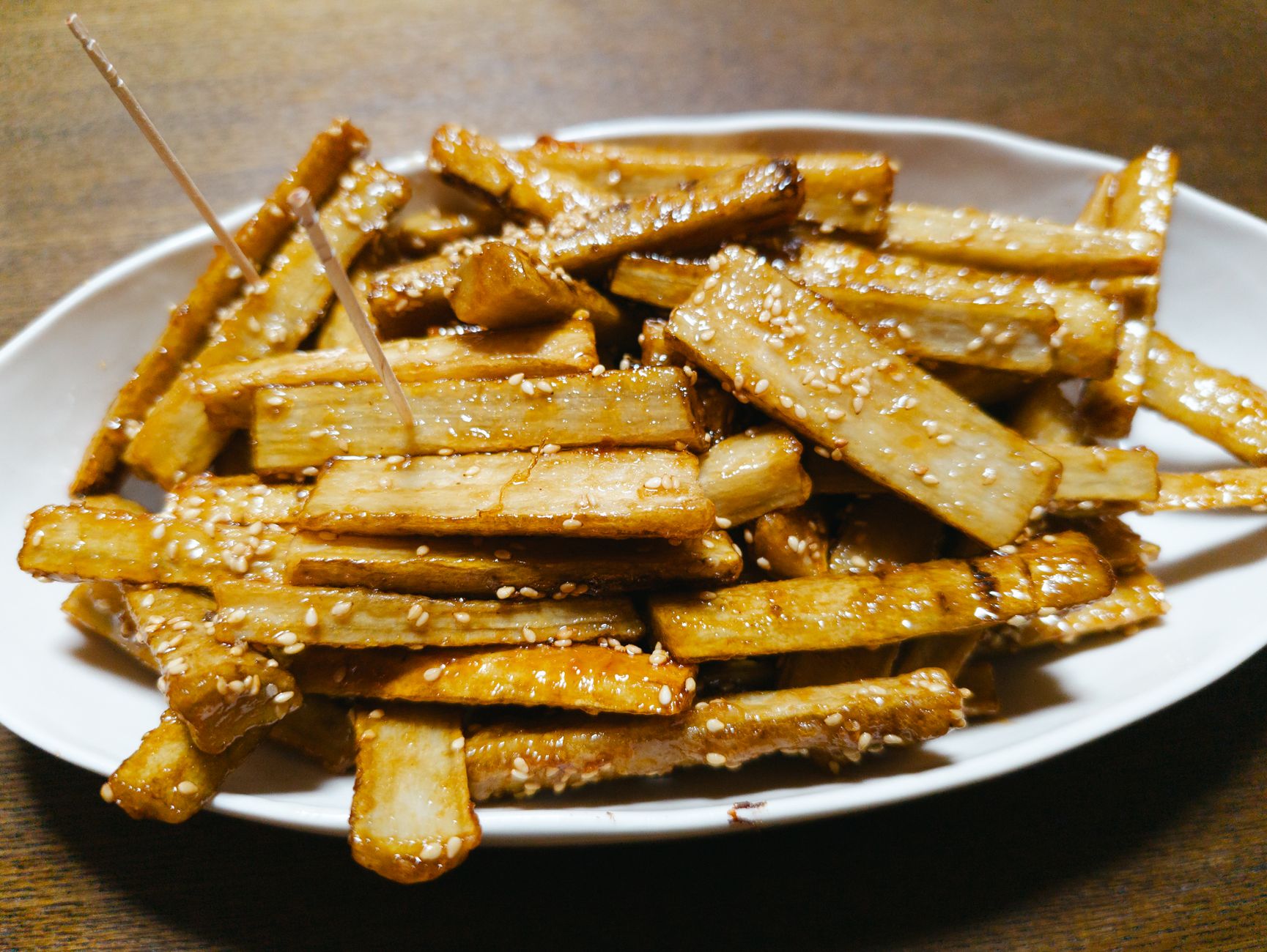 Delicious sesame-coated fried root vegetables served on a white plate, perfect for a tasty meal.