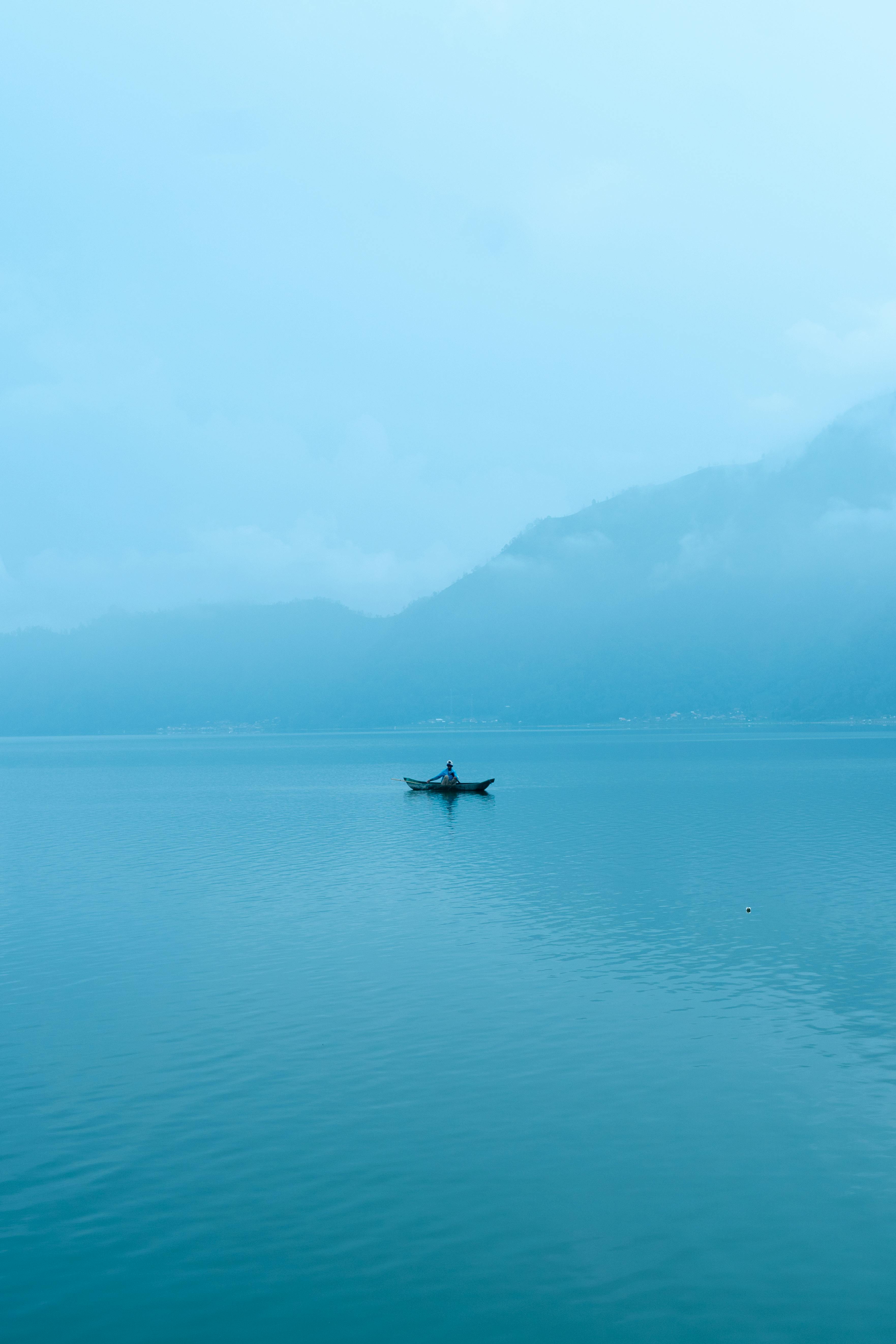 A solitary boat on a calm, misty lake at dawn, evoking a peaceful and mysterious ambiance.