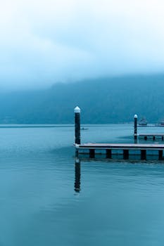 Calm lake scene with piers and misty mountains reflecting over water, perfect tranquil setting.
