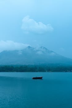 A serene scene of a lone boat on a foggy lake, with mountains in the background, capturing a peaceful atmosphere.