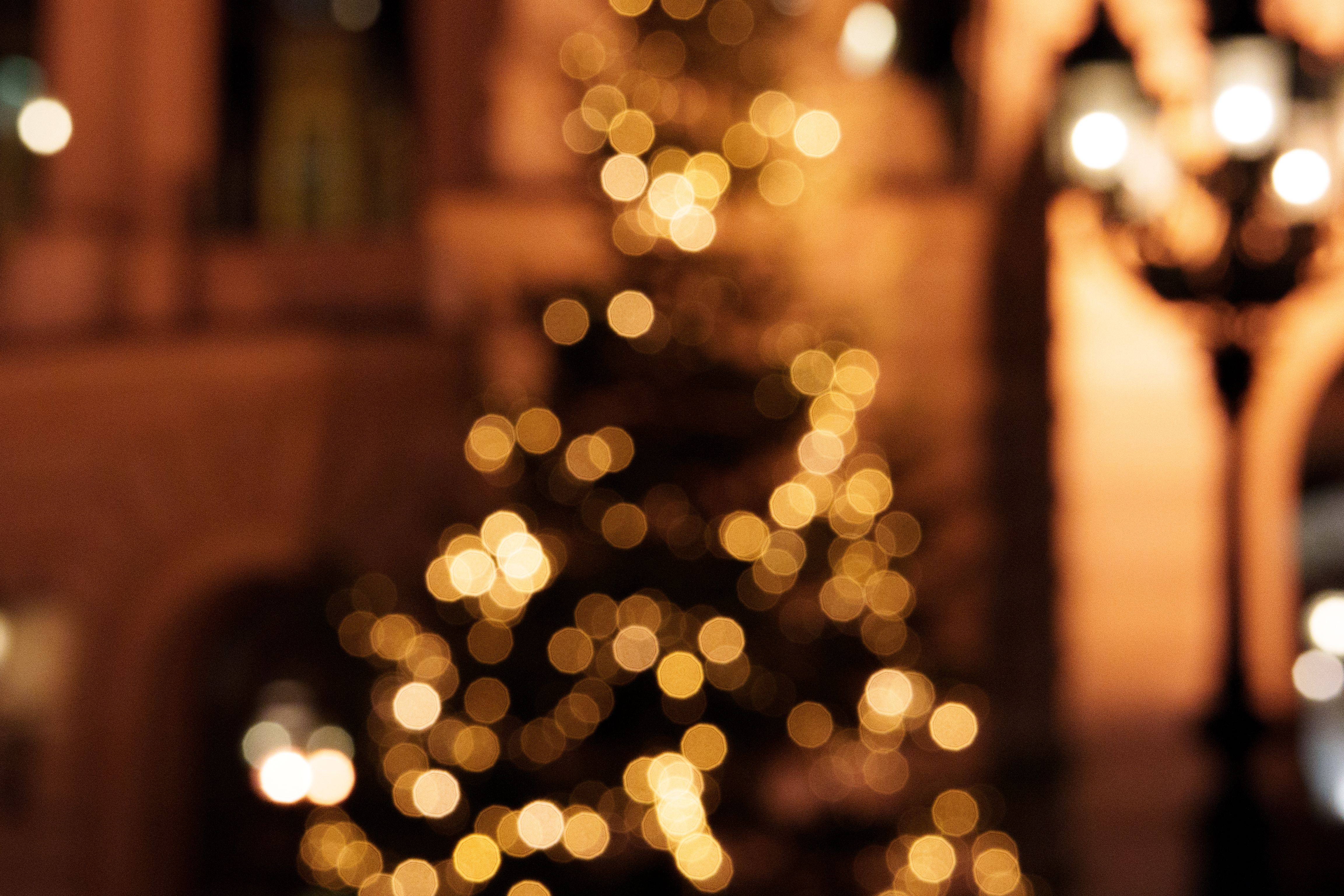 Blurred image of a Christmas tree with warm glowing lights in an urban night setting.