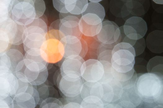 A close-up abstract image featuring defocused white, grey, and orange bokeh lights.
