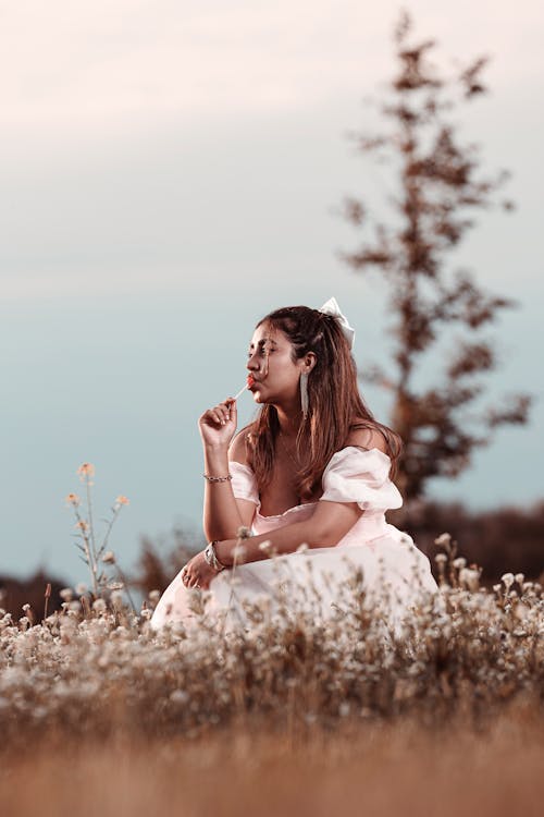 Woman in White Dress Sitting with Lollipop on Meadow