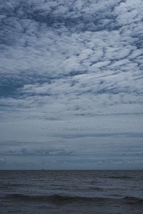 Free Calm ocean waves beneath a dramatic cloud-filled sky, captured at dusk, offering a tranquil and moody atmosphere. Stock Photo