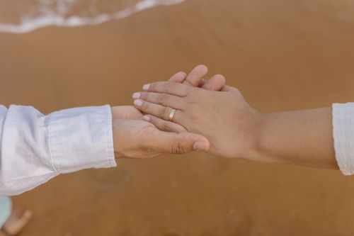 Free Close-up of a couple holding hands on a sandy beach, showcasing a wedding ring. Stock Photo