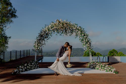 Bride and Groom Standing under an Arch Decorated with Flowers 