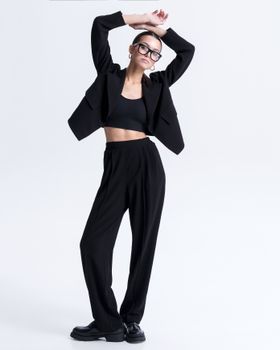 Stylish woman in a black outfit posing in a studio with a white background.
