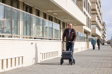 Elderly man strolling with a rollator on a city sidewalk, showcasing urban mobility.