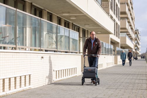 Elderly Man Walking on a Sidewalk with a Rollator with a Shopping Bag 