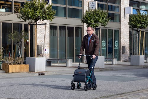 Elderly Man Walking on a Sidewalk with a Rollator with Attached Shopping Bag