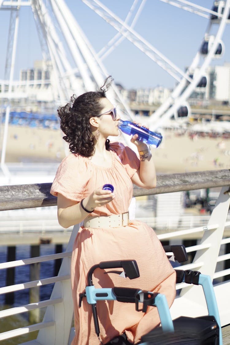 Woman In A Dress Drinking Water On A Pier 