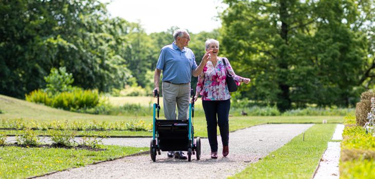 Senior couple walking in a park with a walker, enjoying a sunny day outdoors.