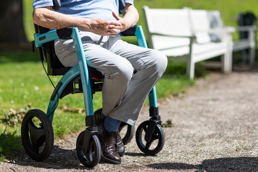 Senior man sitting on a rollator in a sunny park, symbolizing active aging and mobility assistance.