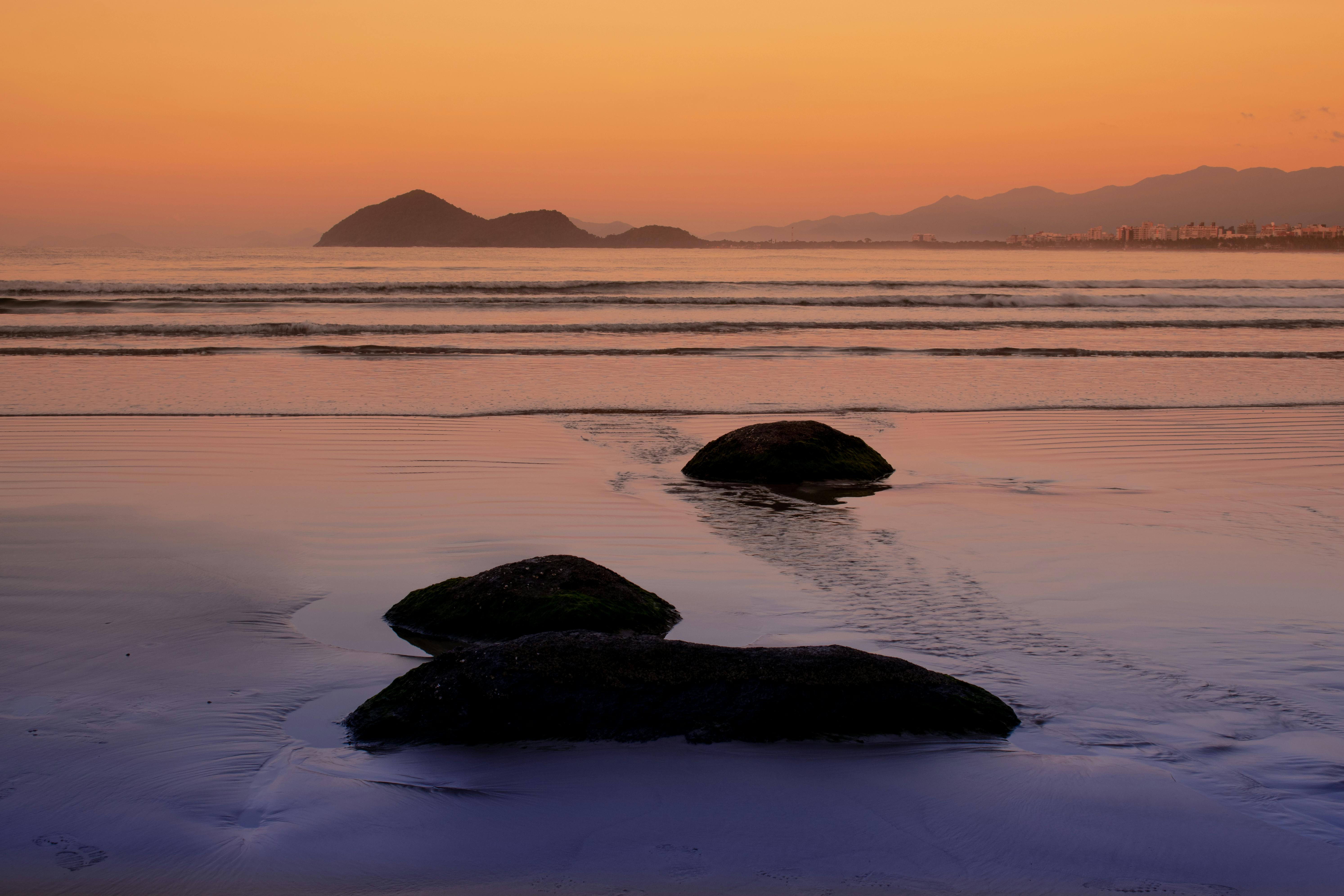 Peaceful seaside scene at sunset with calm waves and distant island view.