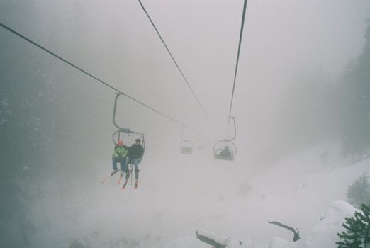 Misty ski lift journey through snowy mountains with skiers during winter.