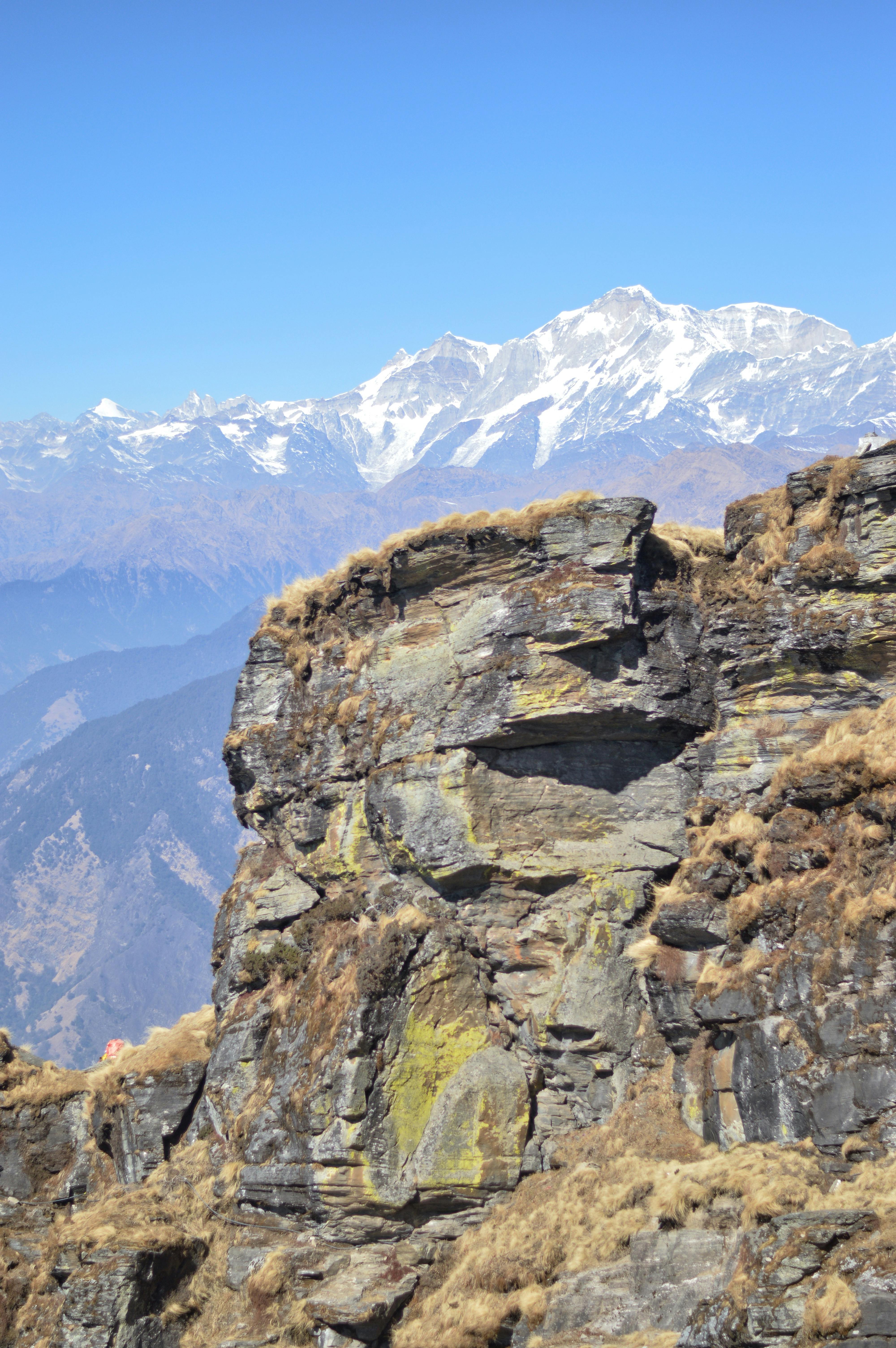 Spectacular view of a rocky cliff against snowcapped mountains under a clear blue sky.