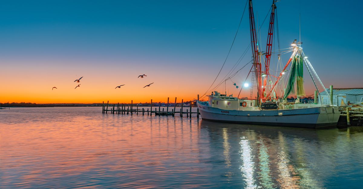 A fishing boat docked at sunset in Swansboro Harbor, North Carolina, with vibrant sky and calm waters.