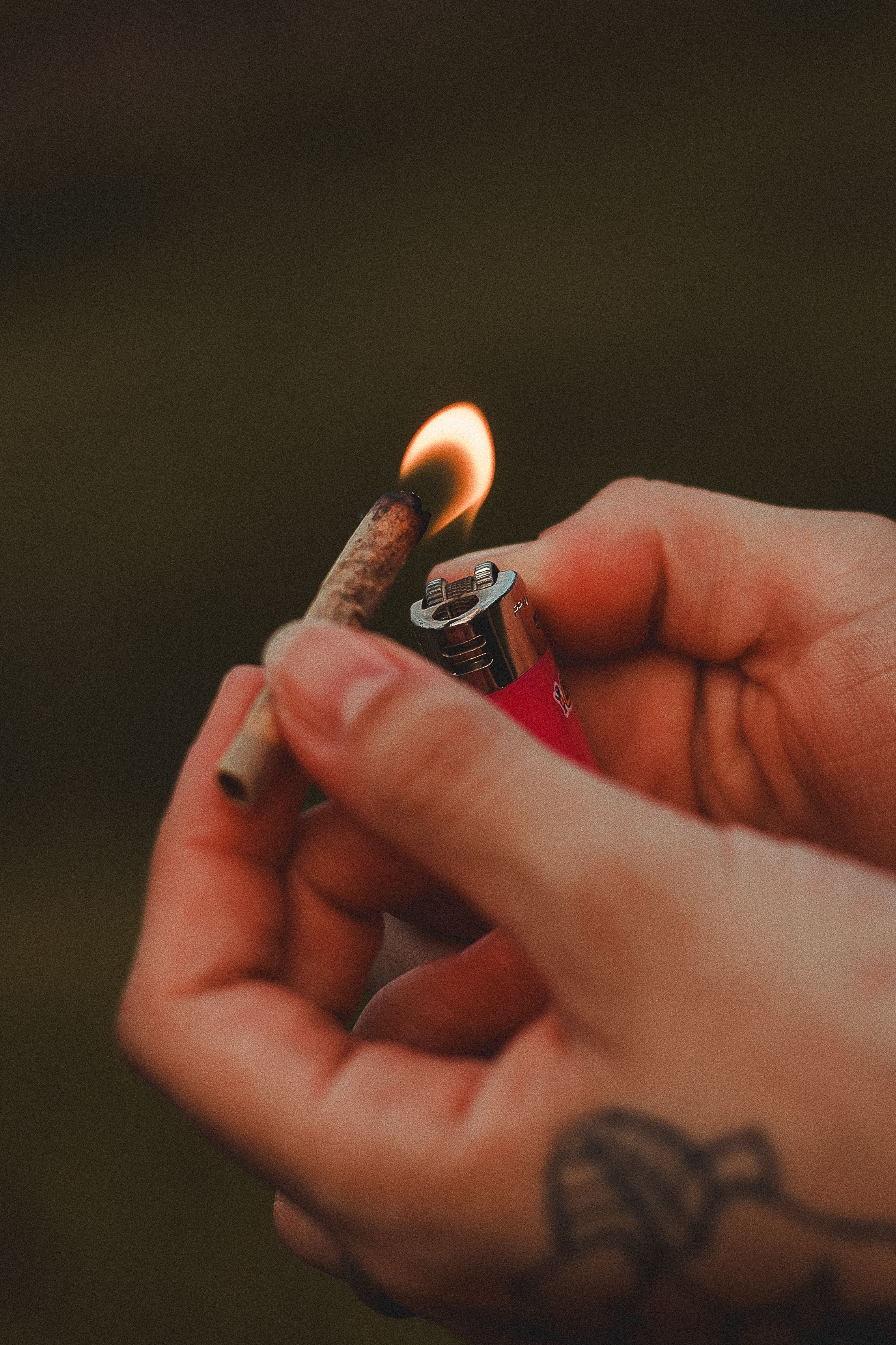 Close-up of hands lighting a joint with a lighter, showcasing tattoos.