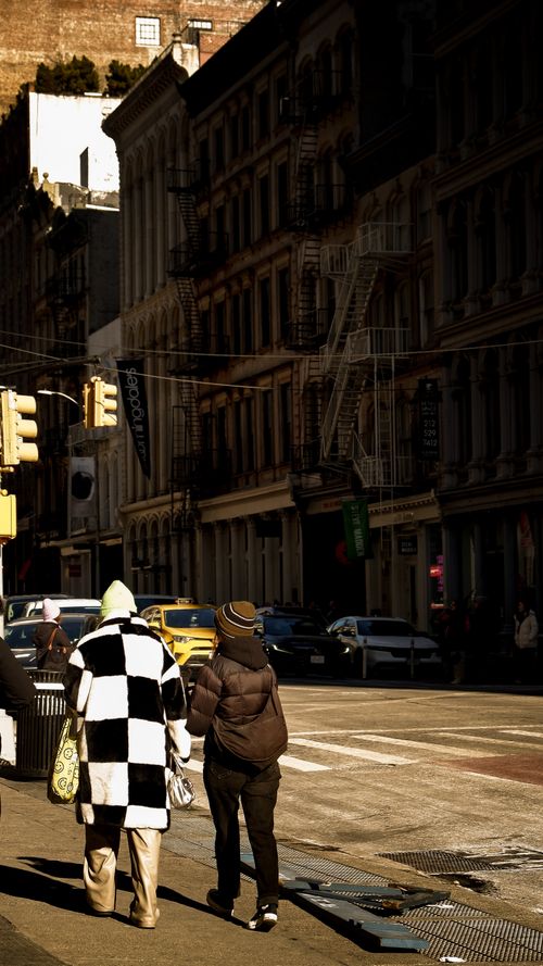 Free Two people walk along a city street with classic buildings, bathed in winter sunlight. Stock Photo