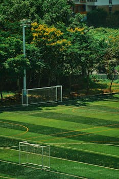 A beautifully green soccer field with goalposts, surrounded by lush trees. Ideal for sports themes.