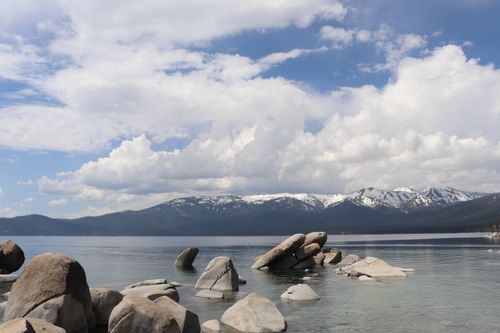 Free Tranquil scene of a clear mountain lake, rocks, and snow-capped peaks under a blue sky. Stock Photo