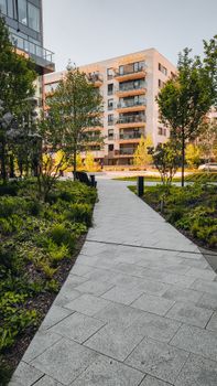 A tranquil modern residential pathway surrounded by trees and greenery with modern apartments in the background.