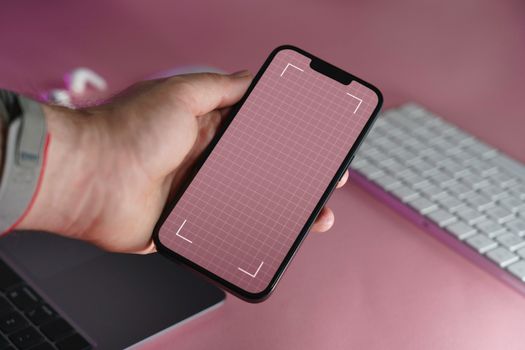 A person holding a smartphone with a blank grid screen and keyboard in the background.