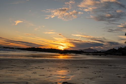 Free Peaceful beach scene at sunset with vibrant colors and reflections on the sand. Stock Photo