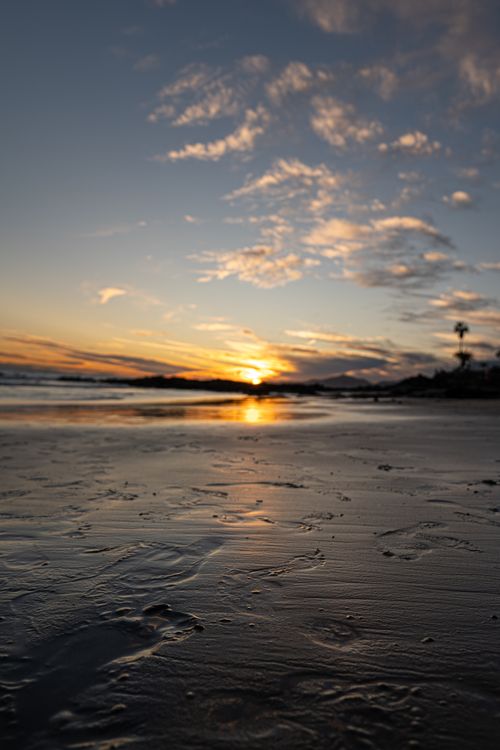 Free Peaceful beach scene at sunrise with reflective waters and a colorful sky. Stock Photo
