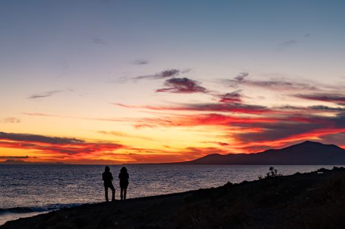 Free Silhouette of a couple standing by the ocean during a vibrant sunset, creating a romantic ambiance. Stock Photo
