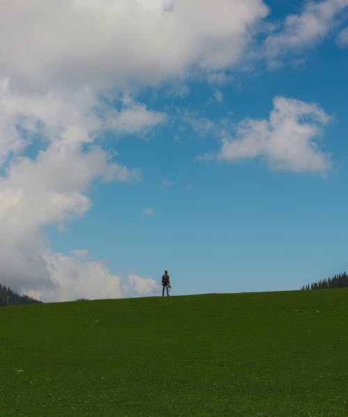 A person is standing on a green field with a blue sky