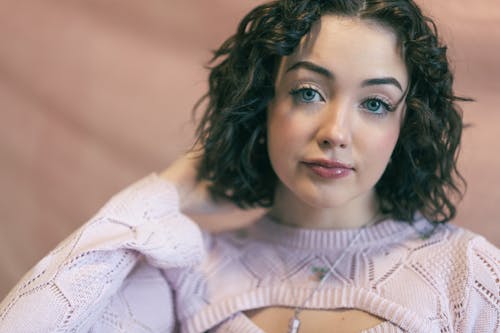 A woman with curly hair wearing a pink sweater