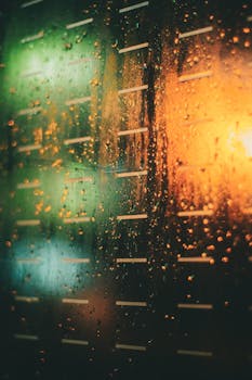 Close-up of raindrops on a window illuminated by colorful night lights.