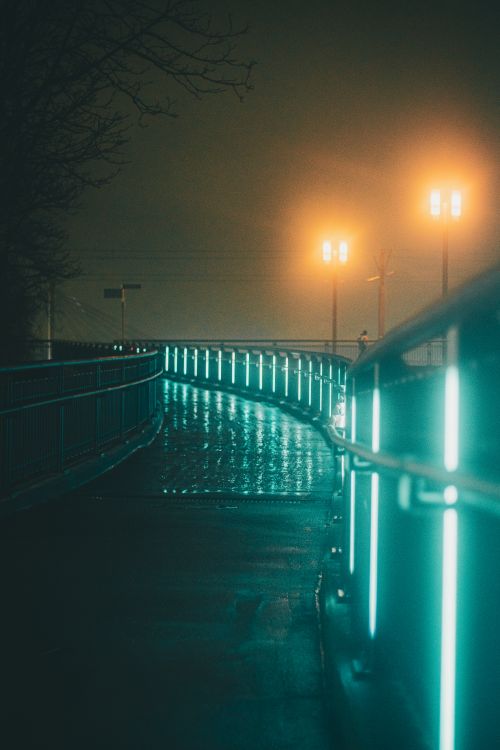 Free A moody night scene of an illuminated urban bridge shrouded in fog with glowing streetlamps and reflections. Stock Photo
