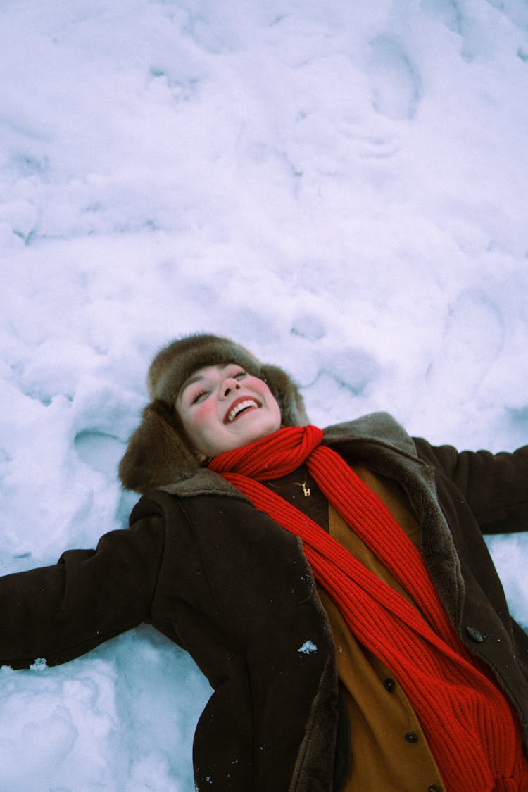 Smiling Woman In Scarf And Coat Lying Down In Snow