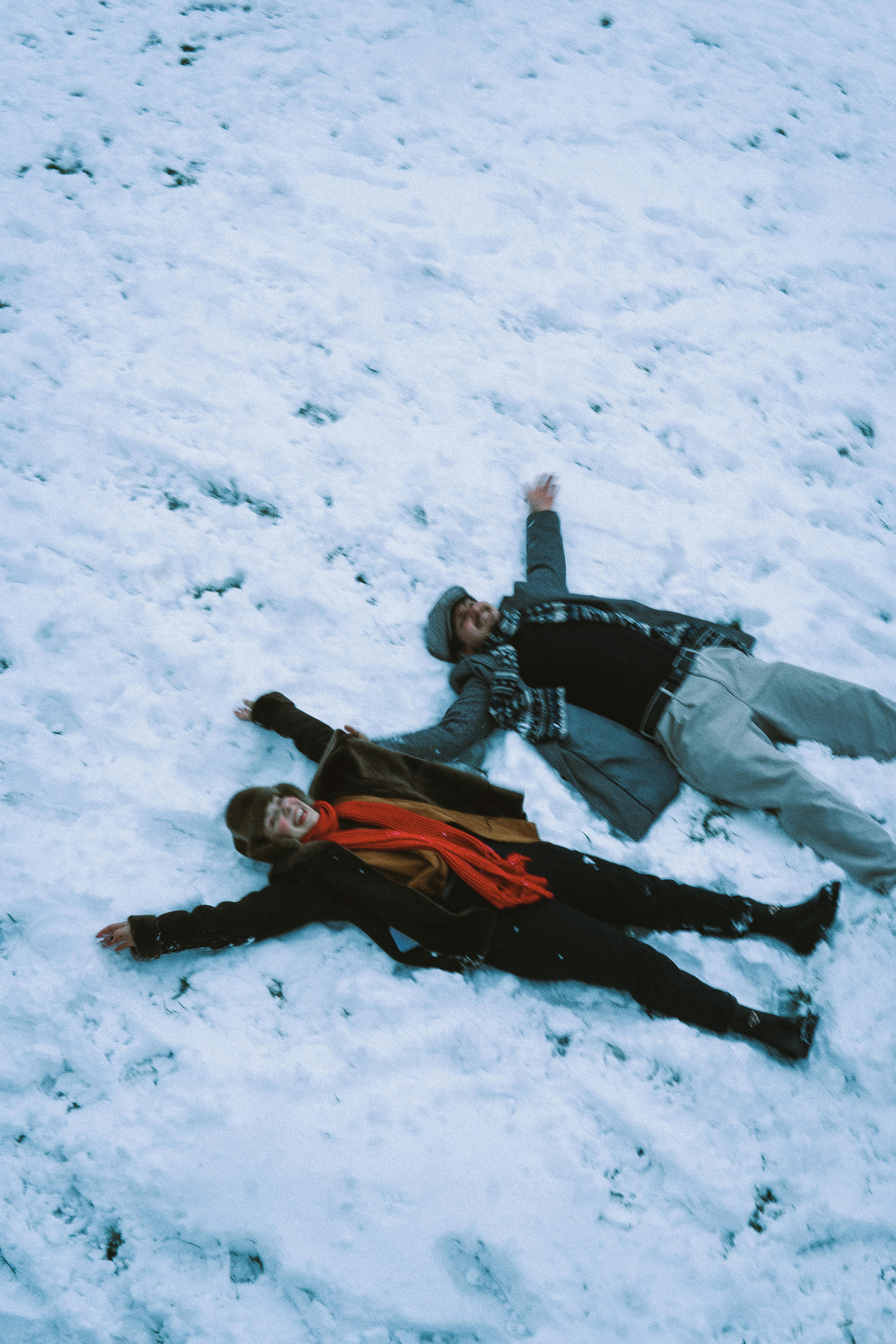 A happy couple making snow angels on a snowy field in Baku, capturing the joy of winter.