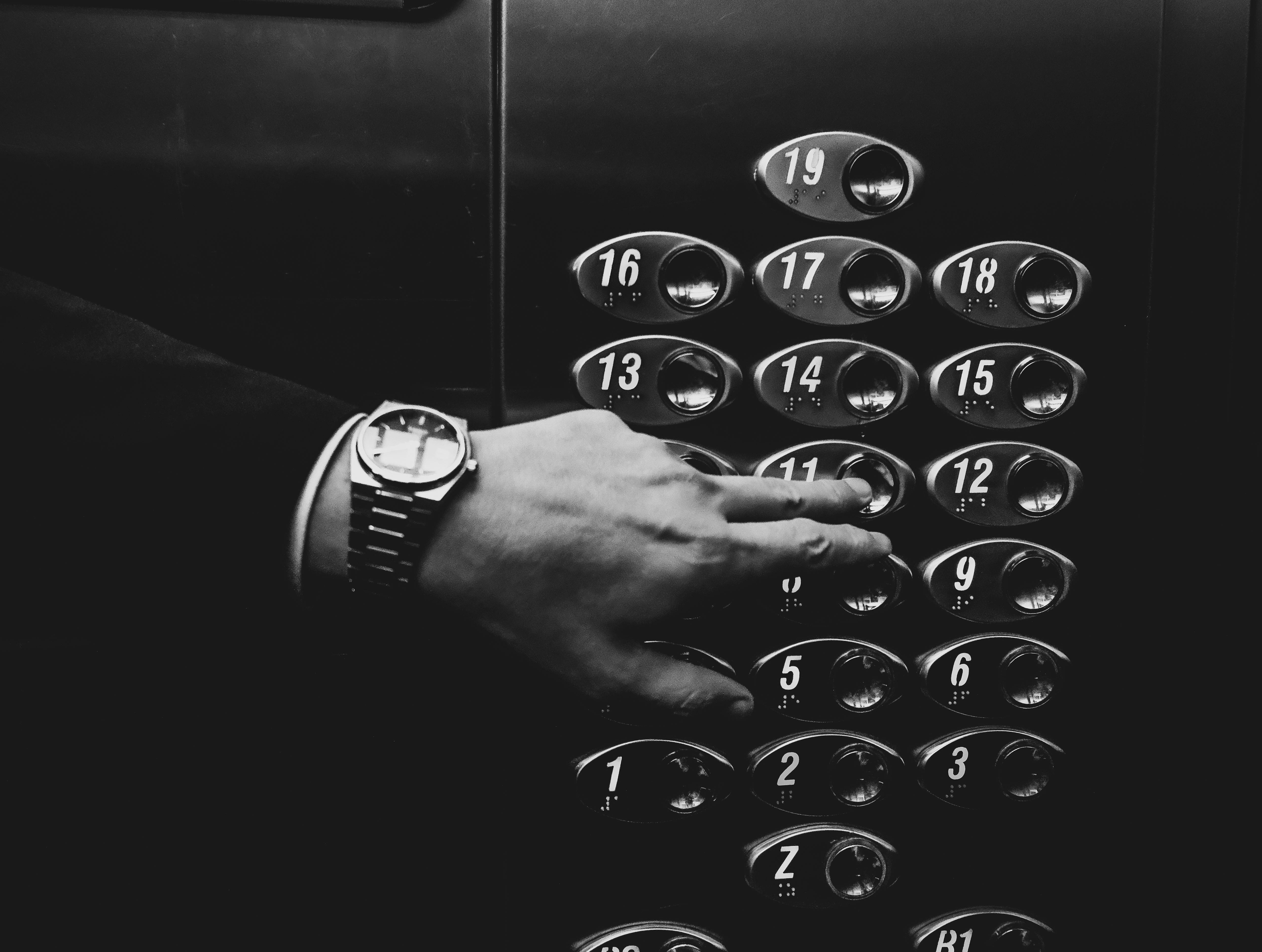 A person's hand with a wristwatch pressing an elevator button in a stylish indoor setting.