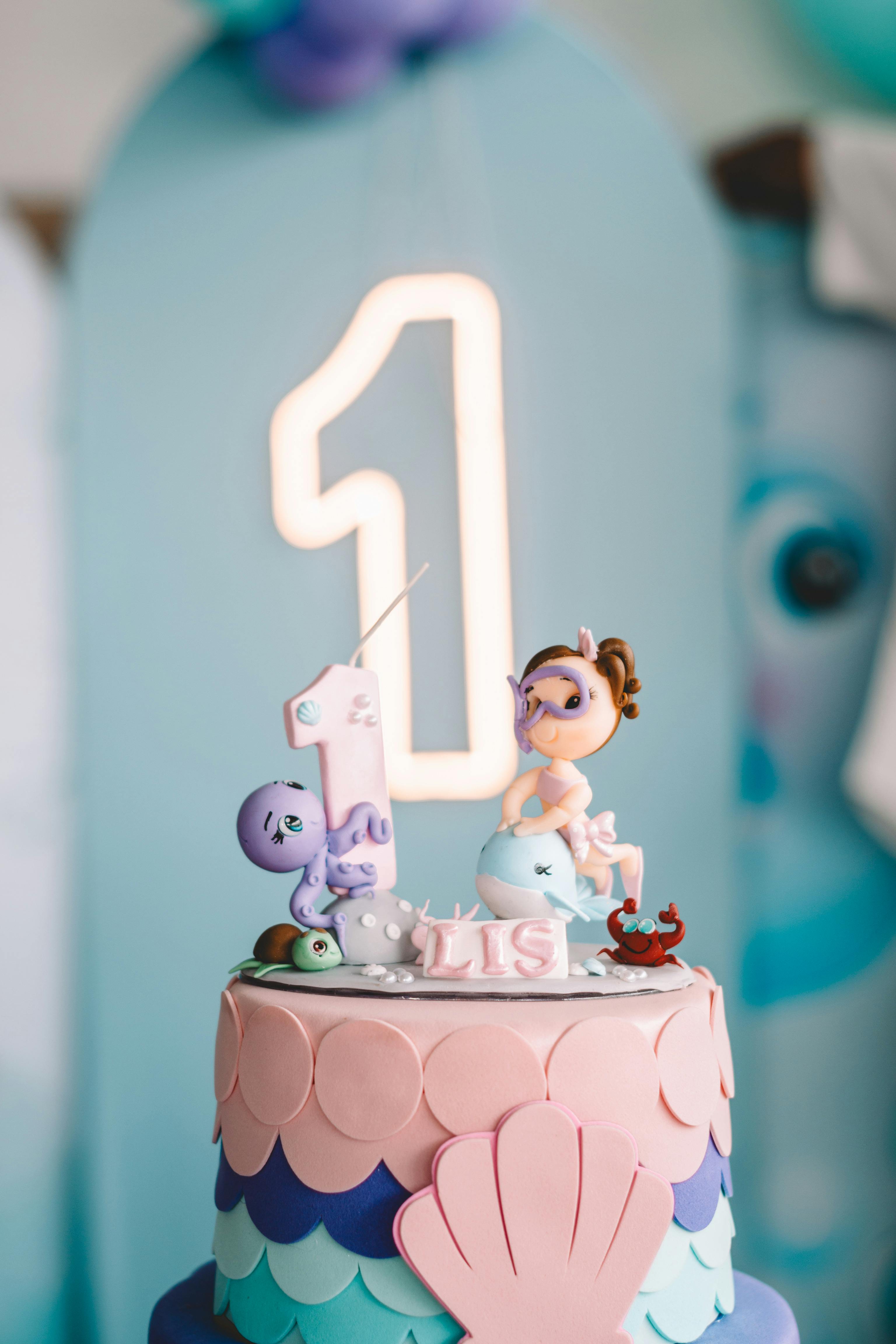 Whimsical under the sea themed birthday cake with mermaid topper and pastel decorations, perfect for a first birthday celebration.