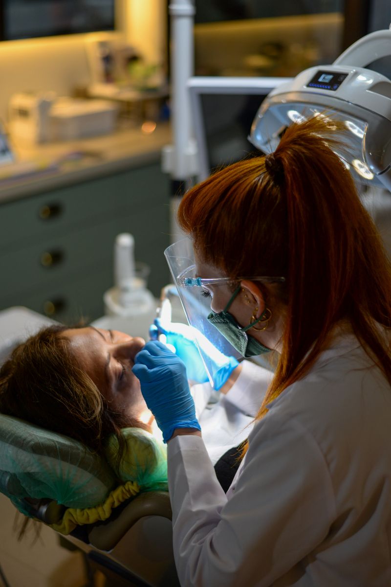 A dentist performing a dental procedure on a patient under bright clinic lights.
