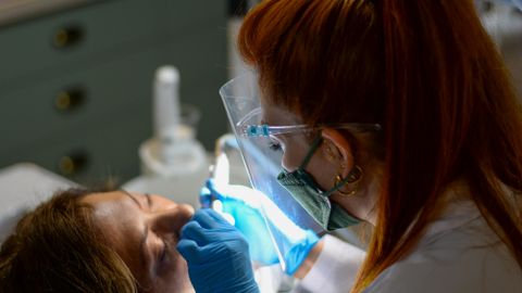 A dentist performing a dental procedure on a patient under bright clinic lights.