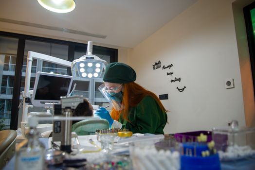 A female dentist in green scrubs performing a dental procedure on a patient in a modern clinic.