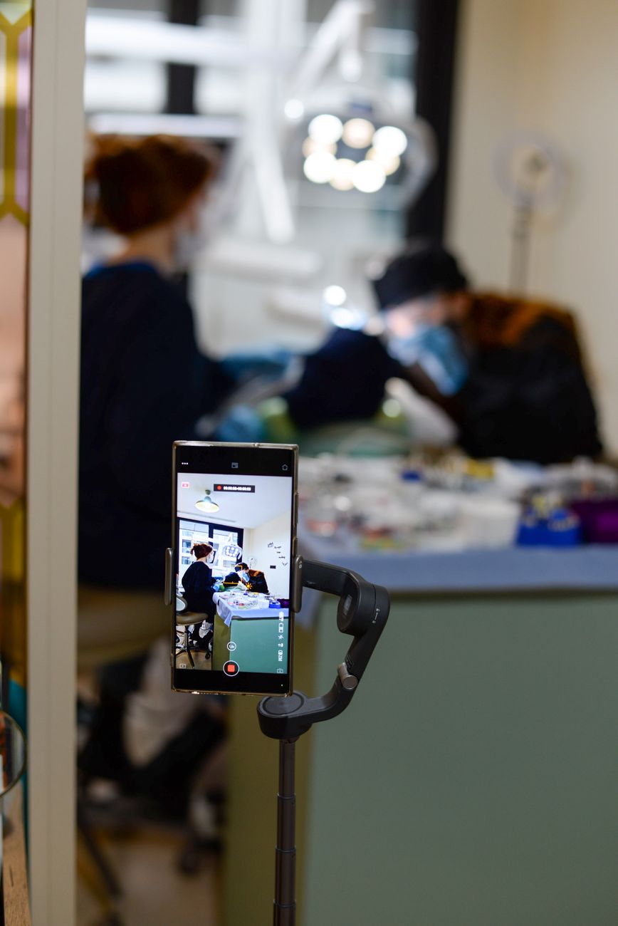 A dental checkup is recorded using a smartphone in a modern clinic setting.