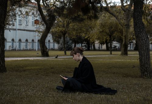 Free Young woman in a black coat reading in a peaceful park environment. Stock Photo